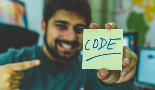 Featured image for javascript cheat sheet blog. It has a man holding up a post it note that says the word code on it.